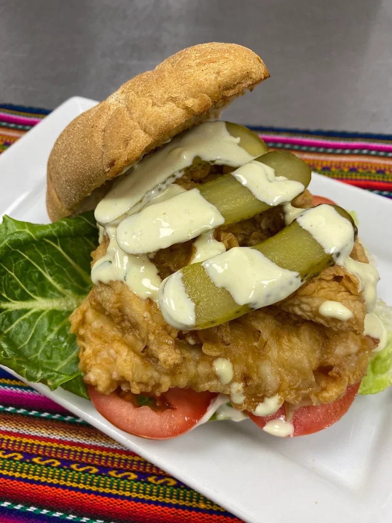 A La Crema sandwich plated with pickles and tomato on a Peruvian textile placemat